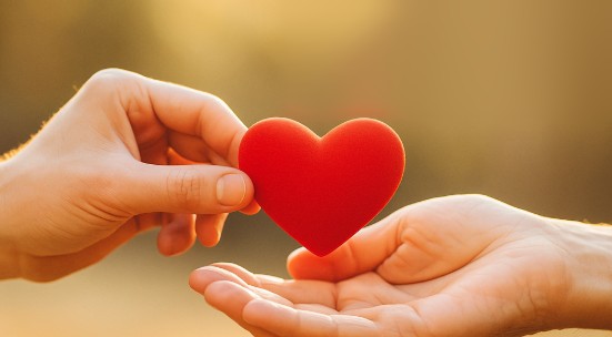 Una mano entrega un corazón rojo a otra mano abierta