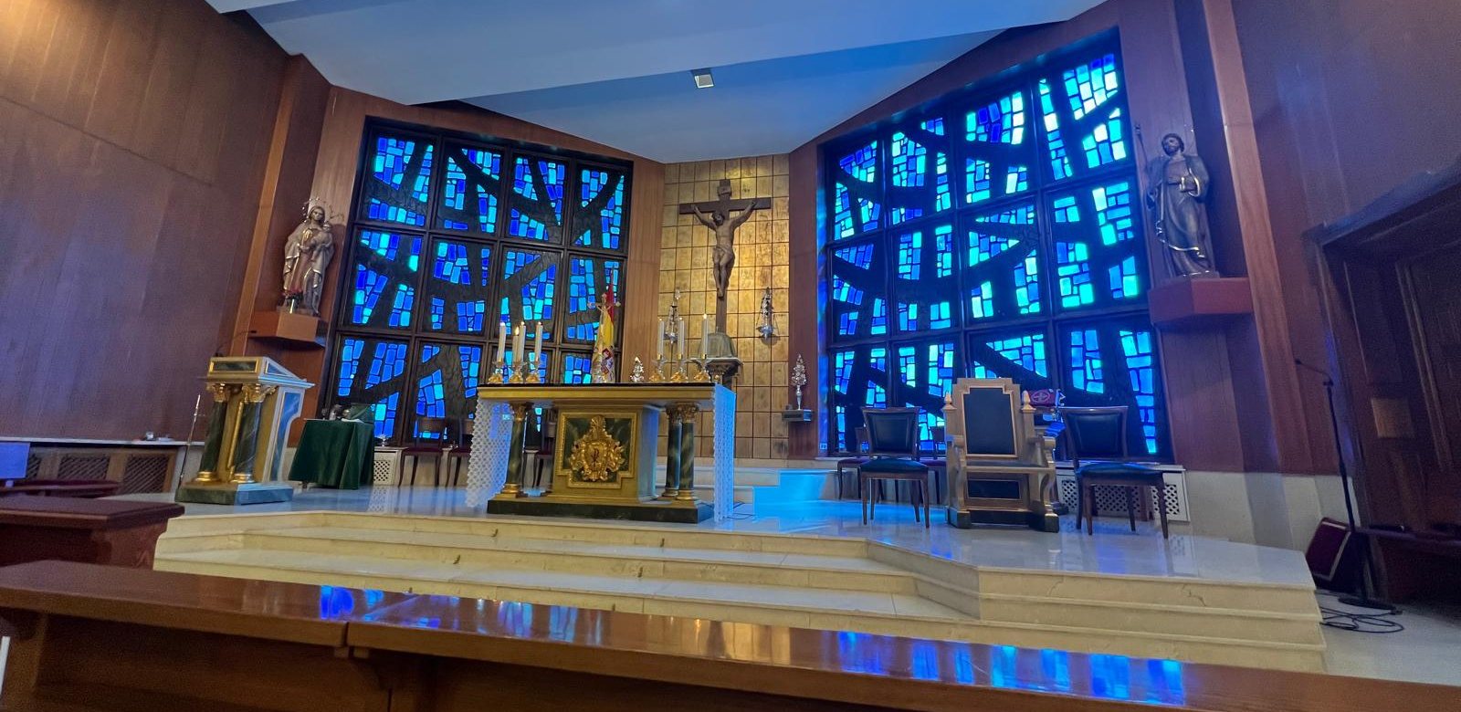Presbiterio de la Parroquia de la Armada: altar, crucifijo sobre fondo dorado y dos grandes vidrieras azules